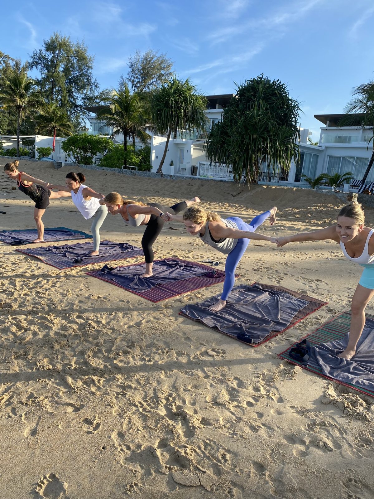 A group of women in a dancer pose chain on a beach at sunrise, holding hands