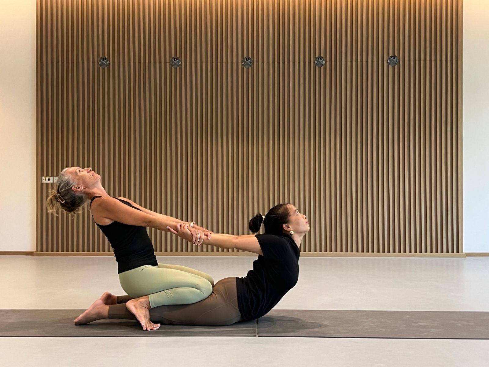 Laurence kneeling on her partner's legs, both leaning back in a supported backbend with joined arms