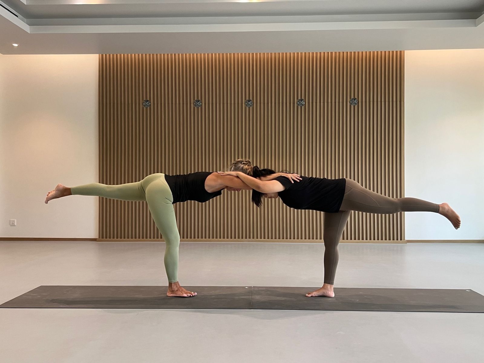 Laurence and a partner in a shared Warrior III balance, arms resting on each other's shoulders