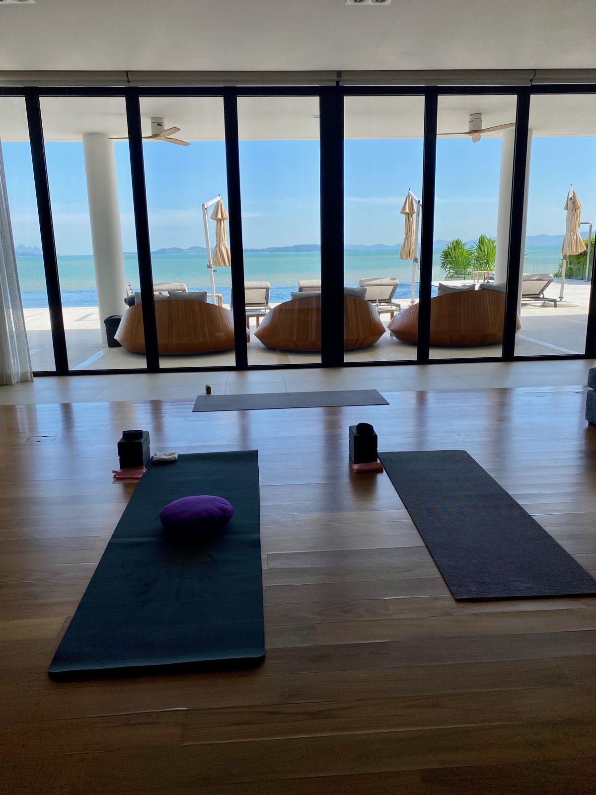 Two yoga mats laid out in a beachfront villa living room, sliding doors open to the Andaman Sea