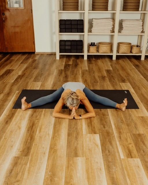 Laurence in a wide-legged forward fold on a wooden floor