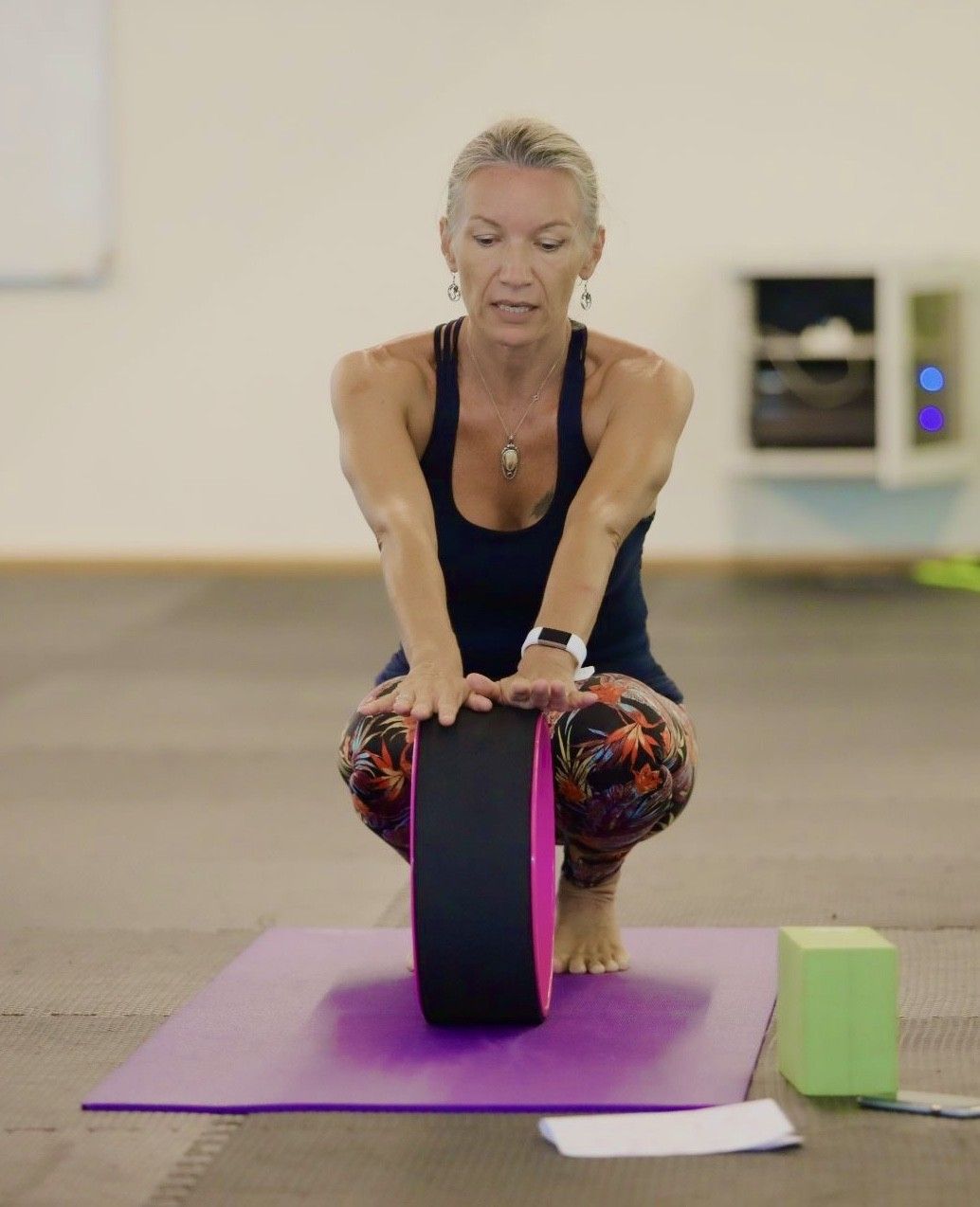 Laurence in a low squat, hands pressed on a yoga wheel on her mat